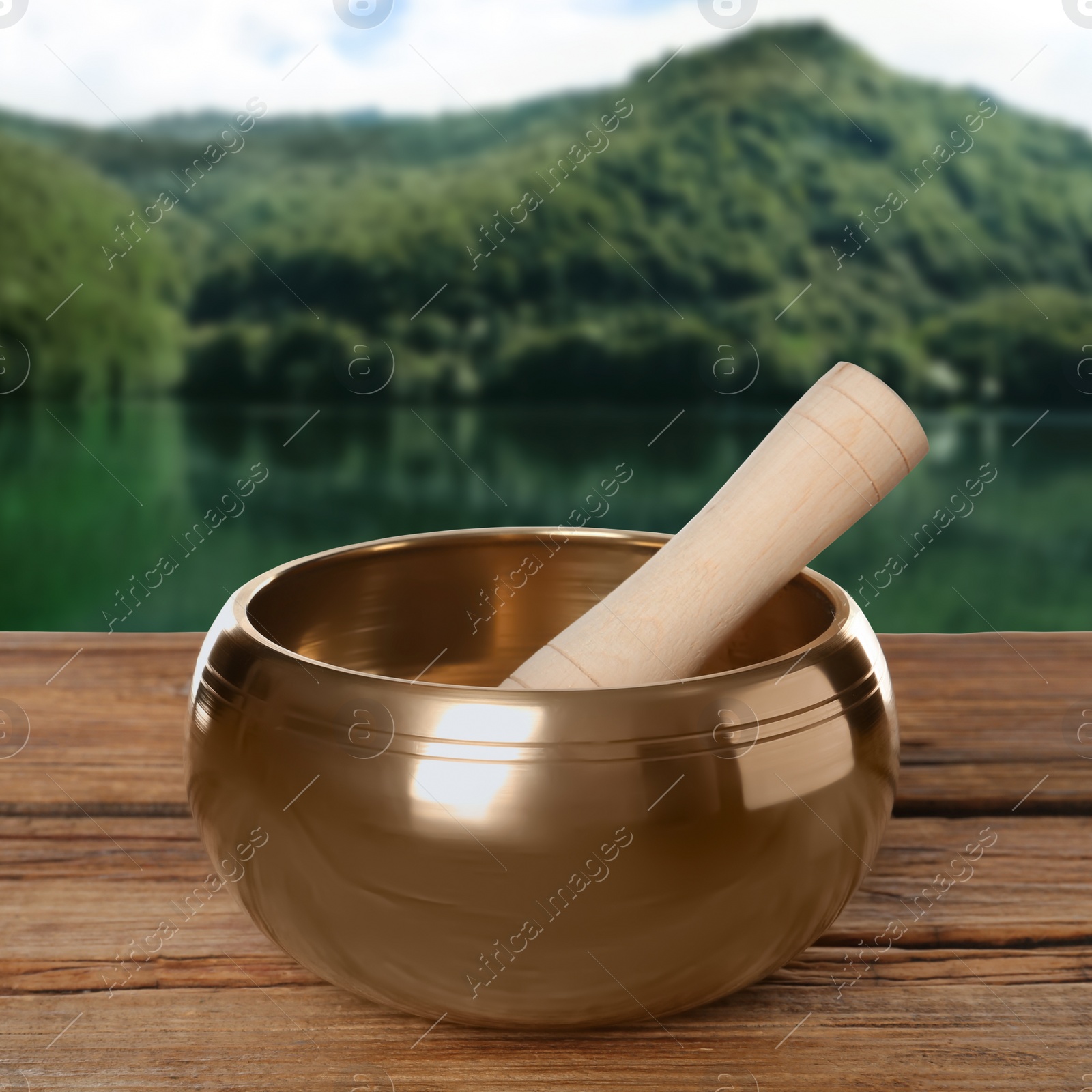 Image of Golden singing bowl and mallet on wooden table against mountain landscape