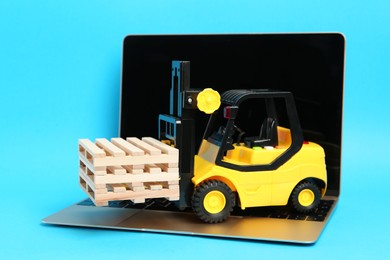 Photo of Laptop and toy forklift with wooden pallets on light blue background