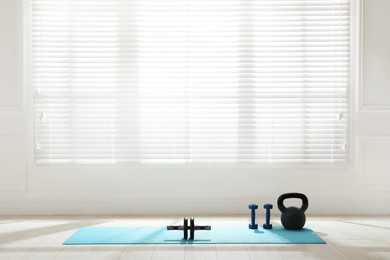 Photo of Exercise mat, ab roller, dumbbells and kettlebell near window in spacious room