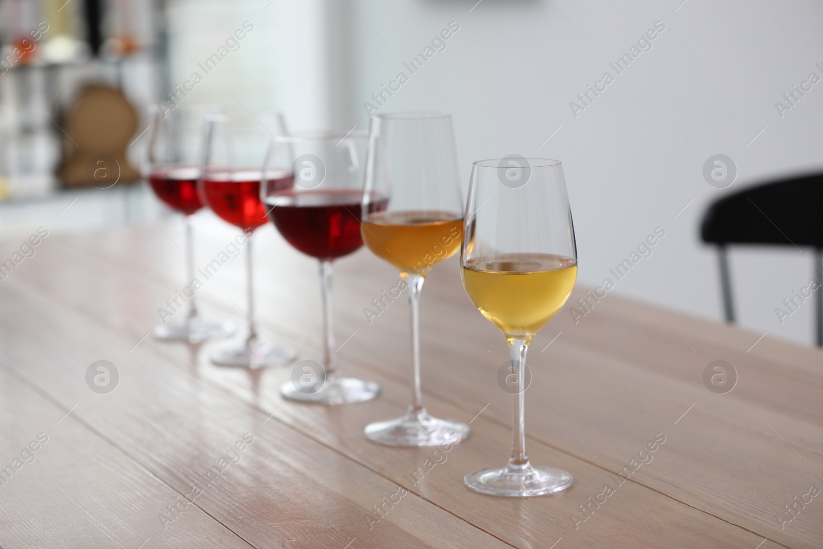 Photo of Different sorts of wine in glasses prepared for tasting on wooden table indoors