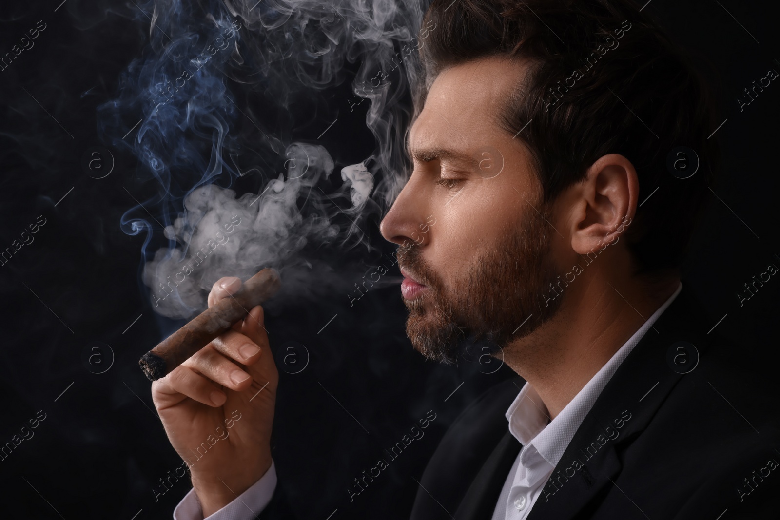 Photo of Handsome man smoking cigar on black background. Space for text