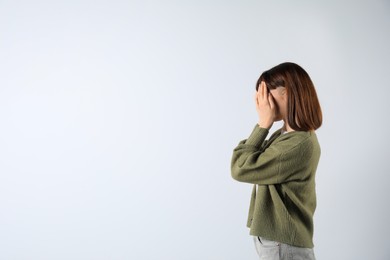 Photo of Young girl hiding face in hands on white background. Space for text