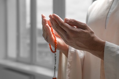 Photo of Muslim man with misbaha praying indoors, closeup. Space for text