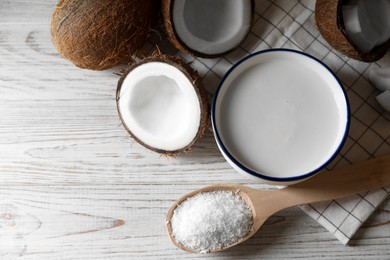 Photo of Bowl of delicious coconut milk, spoon with flakes and nuts on white wooden table, flat lay. Space for text