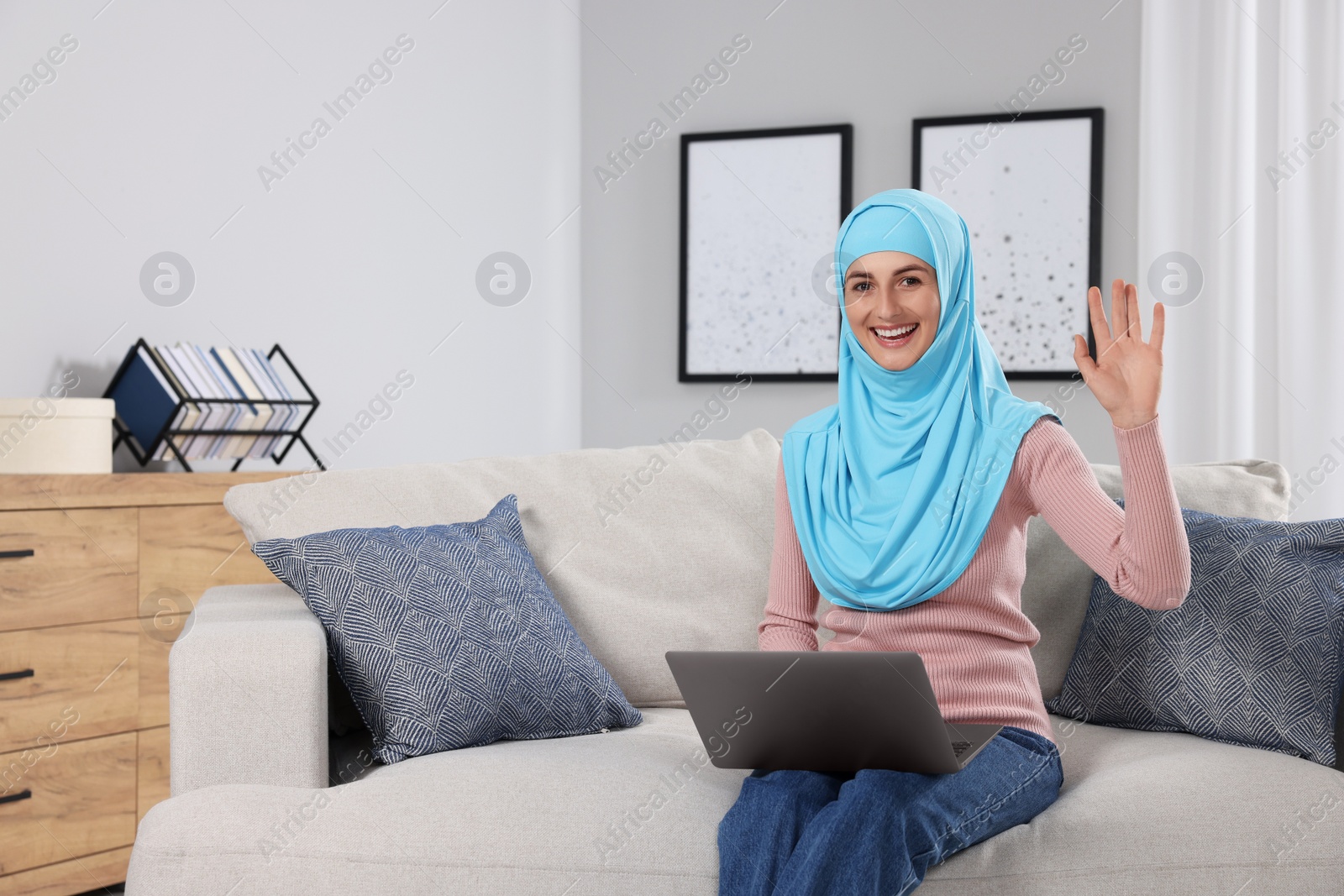 Photo of Muslim woman using laptop at couch in room. Space for text