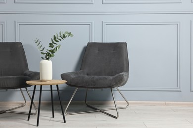 Comfortable armchairs, side table and eucalyptus indoors, space for text