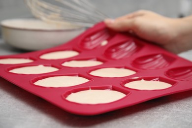 Photo of Woman holding mold for madeleine cookies with batter at grey table, closeup