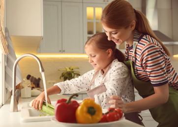 Photo of Mother and daughter washing vegetables in kitchen