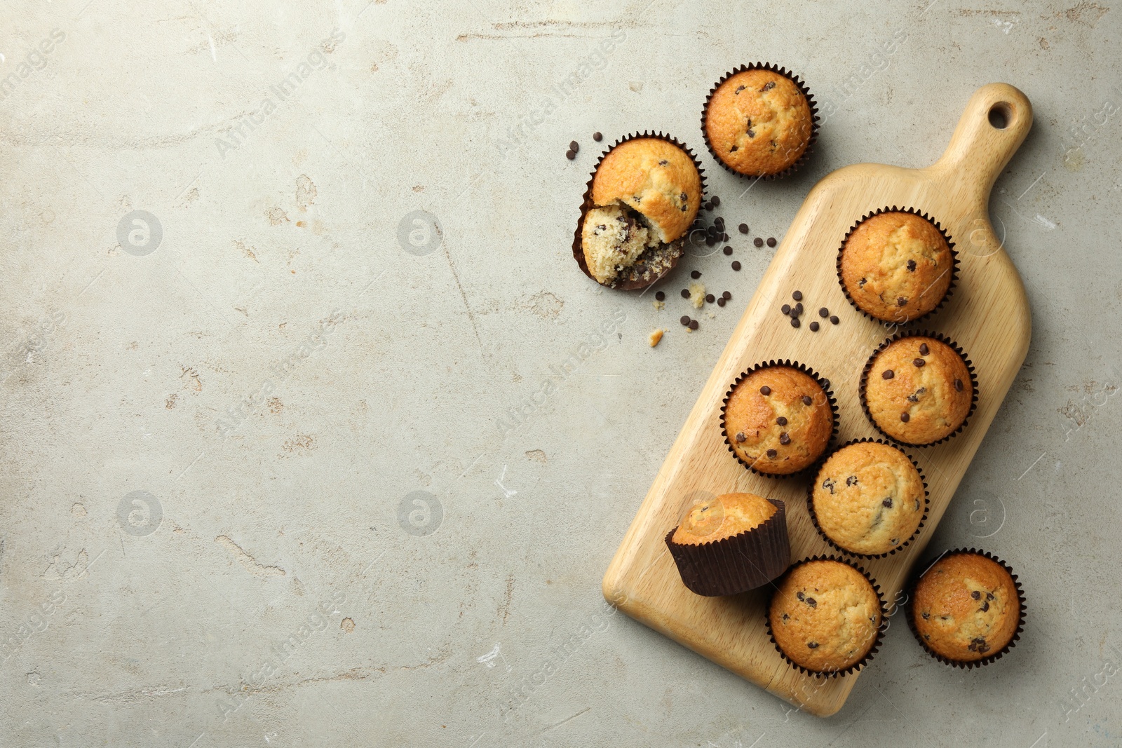 Photo of Delicious sweet muffins with chocolate chips on grey textured table, flat lay. Space for text