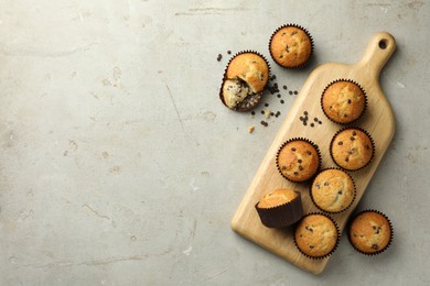 Photo of Delicious sweet muffins with chocolate chips on grey textured table, flat lay. Space for text