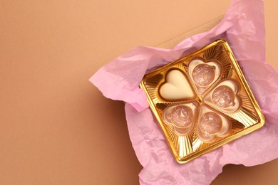 Photo of One heart shaped chocolate candy in box on light brown background, top view. Space for text