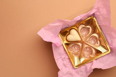 One heart shaped chocolate candy in box on light brown background, top view. Space for text