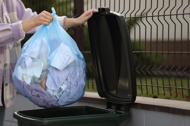 Photo of Woman putting garbage bag into recycling bin outdoors, closeup