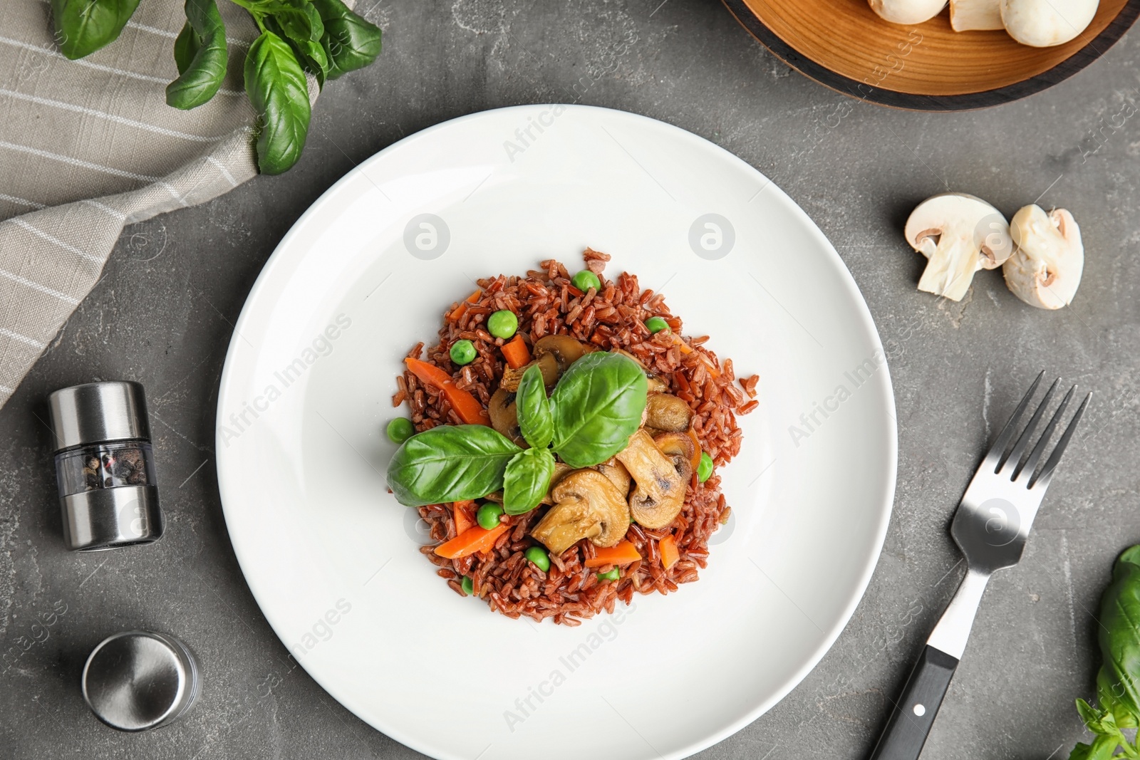 Photo of Plate of tasty brown rice with vegetables and mushrooms on grey table, flat lay