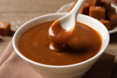 Taking yummy salted caramel with spoon from bowl at table, closeup