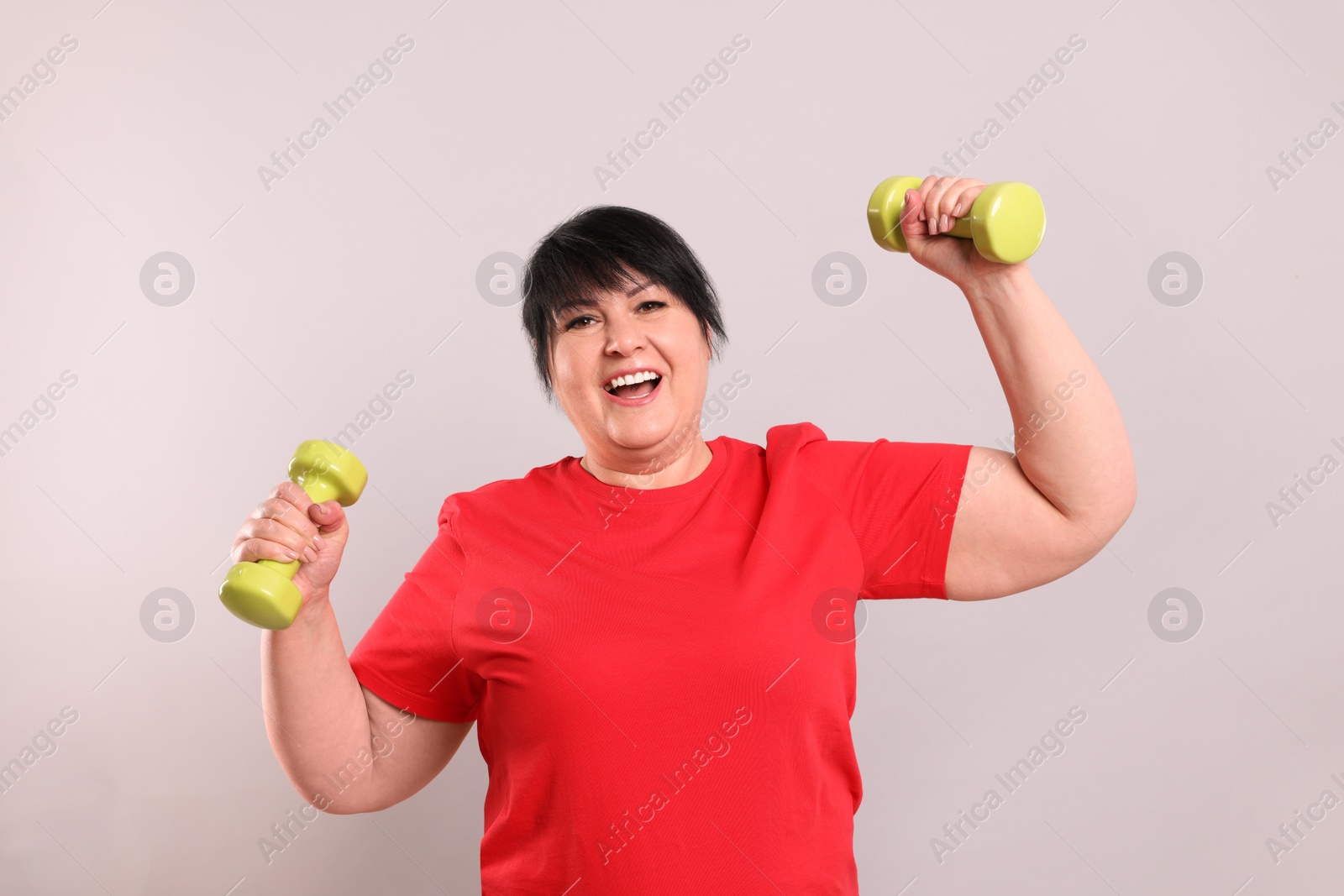 Photo of Happy overweight mature woman doing exercise with dumbbells on grey background