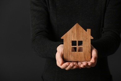 Woman holding wooden house on dark background, closeup. Home insurance