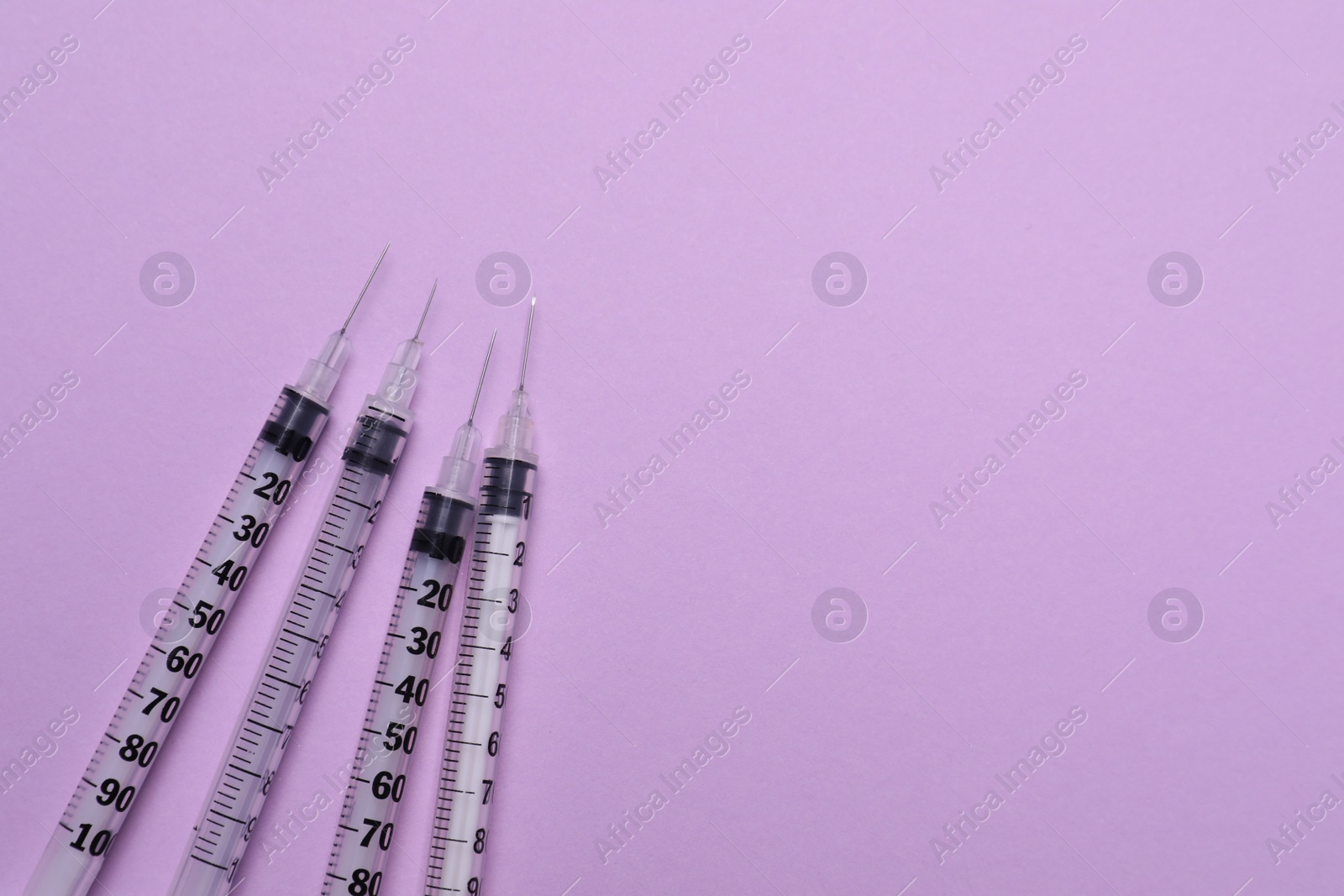 Photo of Disposable syringes with needles on violet background, flat lay. Space for text