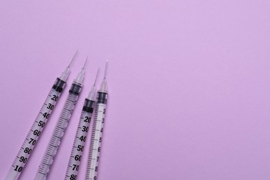 Disposable syringes with needles on violet background, flat lay. Space for text