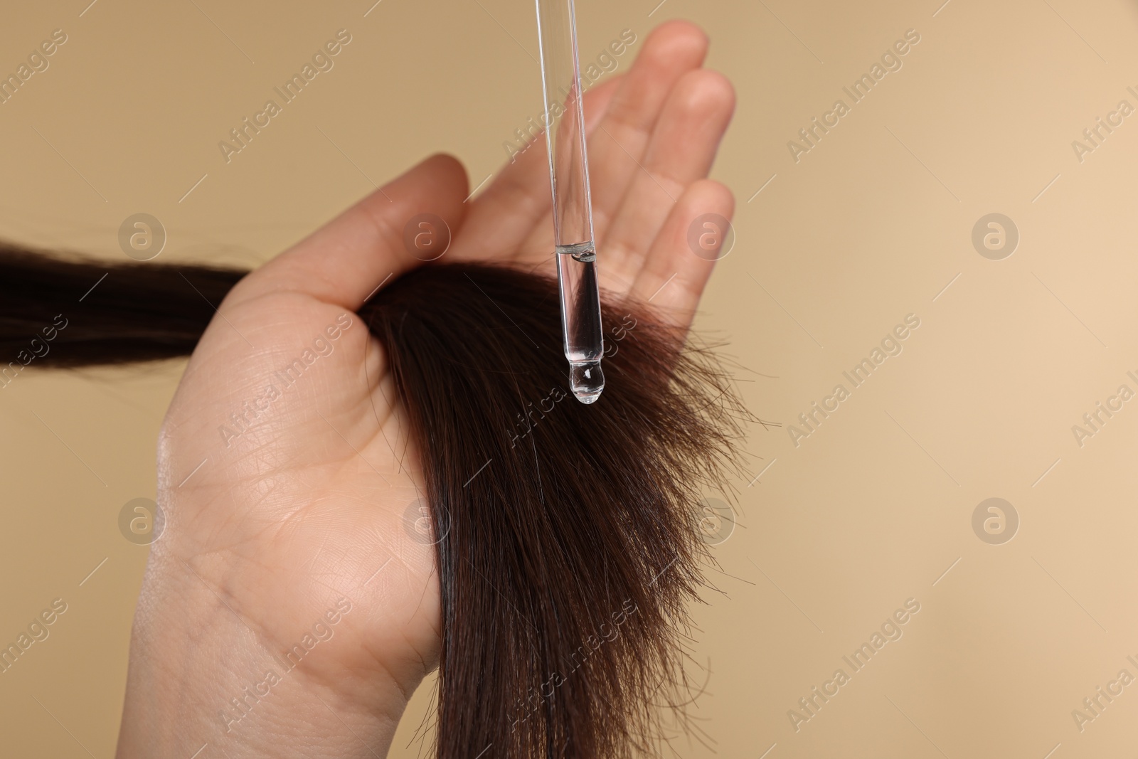 Photo of Woman applying essential oil onto hair on beige background, closeup and space for text