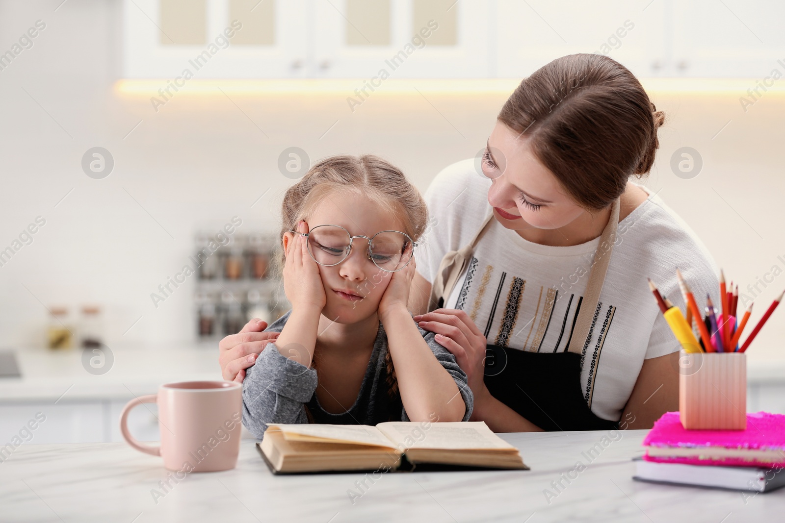 Photo of Woman helping her daughter with homework at table in kitchen