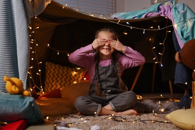 Happy girl covering her eyes in decorated play tent at home