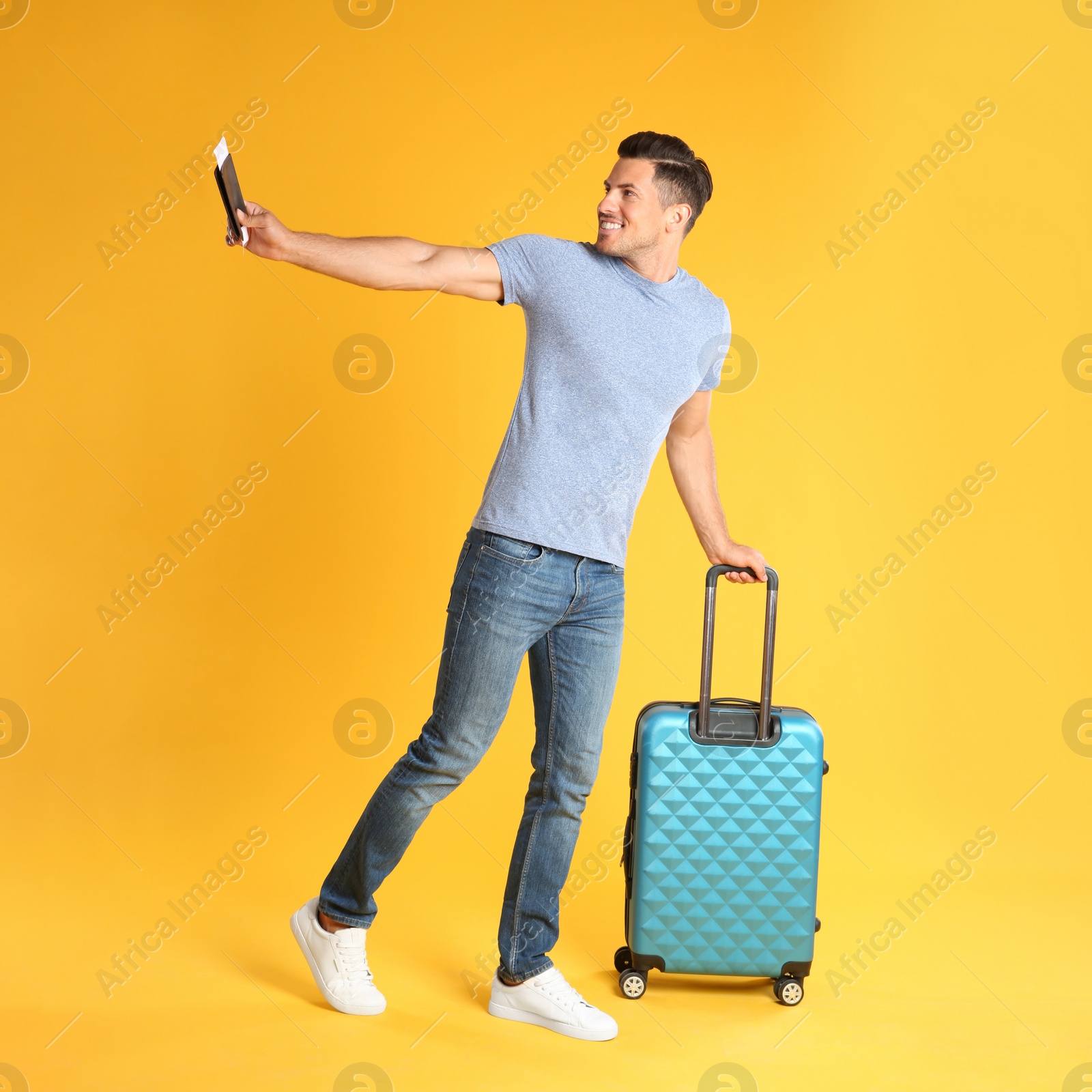 Photo of Handsome man with suitcase and ticket in passport for summer trip on yellow background. Vacation travel
