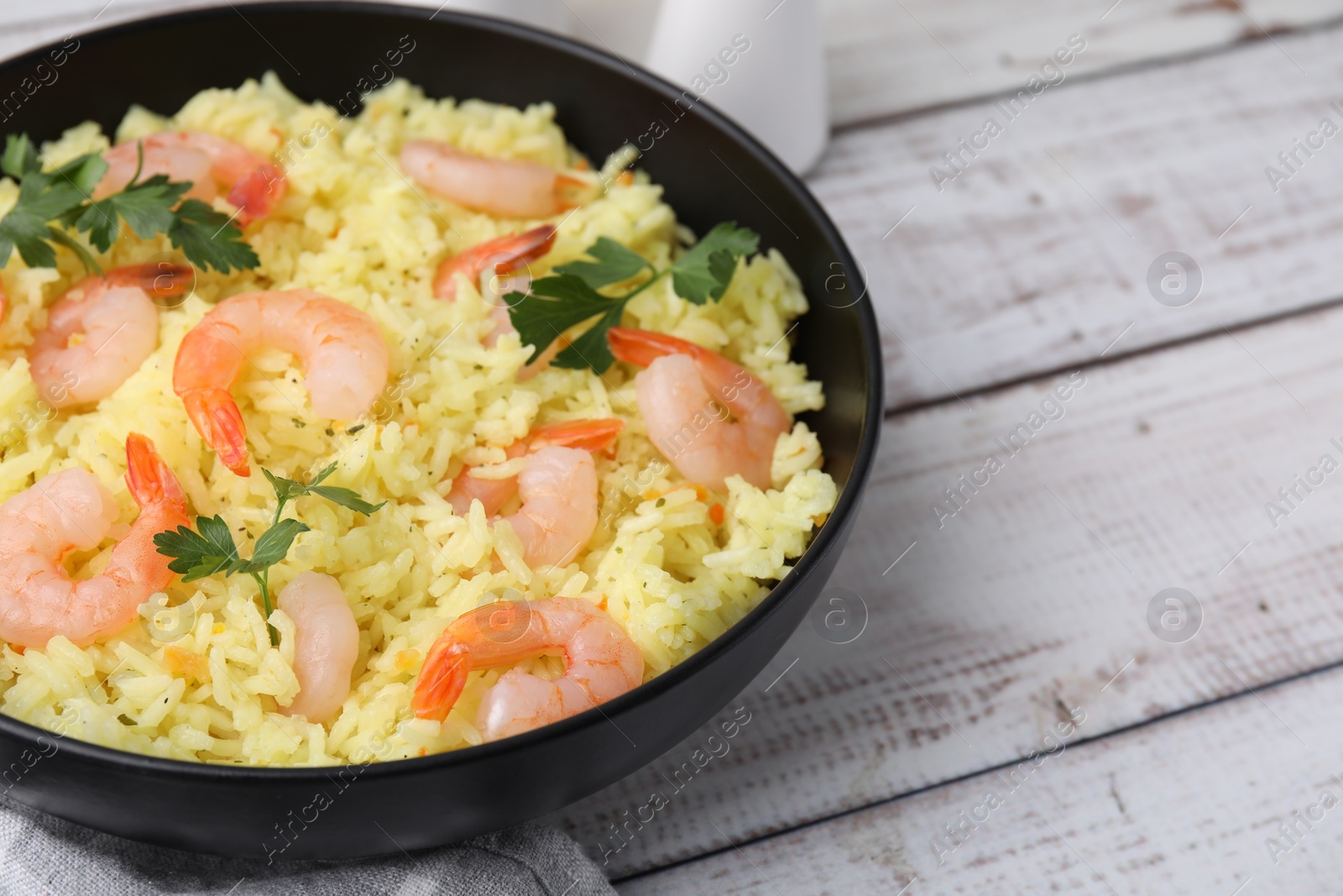 Photo of Delicious risotto with shrimps and parsley in bowl on white wooden table, closeup. Space for text