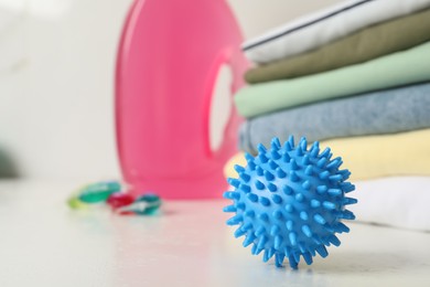 Photo of Blue dryer ball and stacked clean clothes on white table, closeup. Space for text