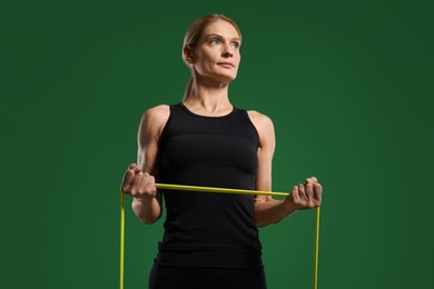 Athletic woman exercising with elastic resistance band on green background, low angle view