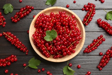 Photo of Delicious red currants and leaves on dark wooden table, flat lay