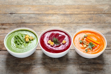 Photo of Various cream soups in bowls on wooden table. Space for text