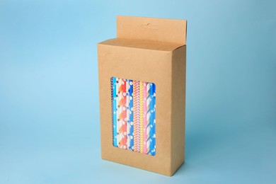 Photo of Box with many paper drinking straws on light blue background
