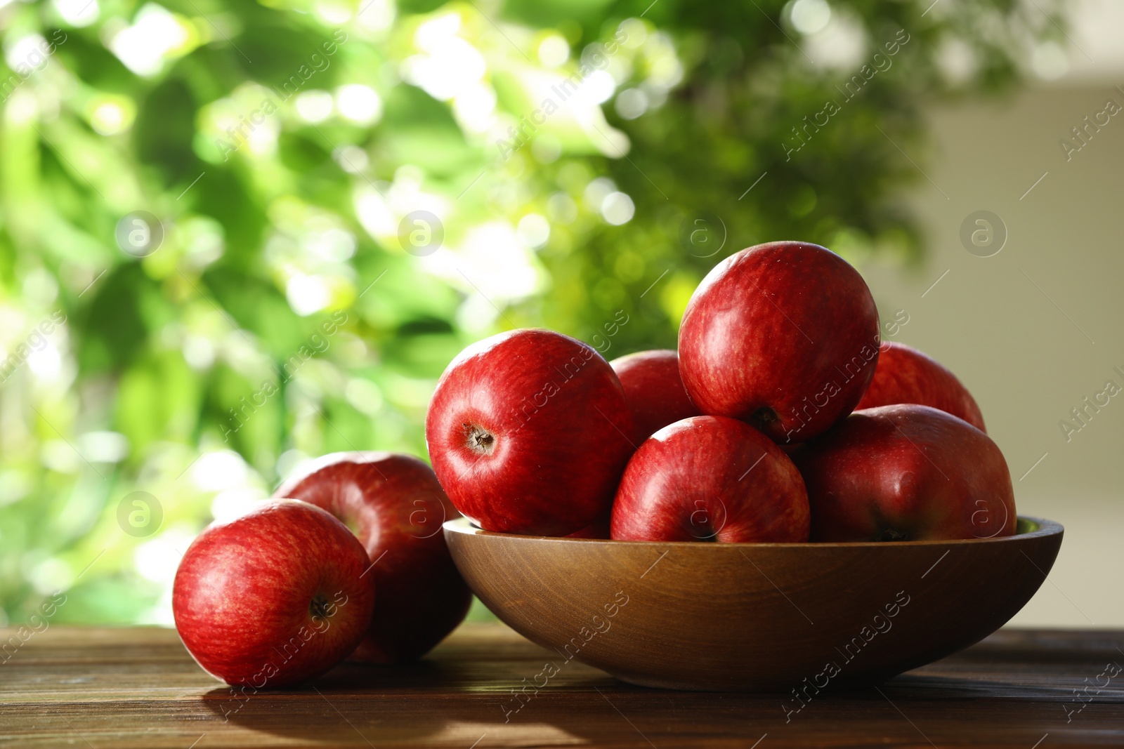 Photo of Ripe red apples and bowl on wooden table outdoors