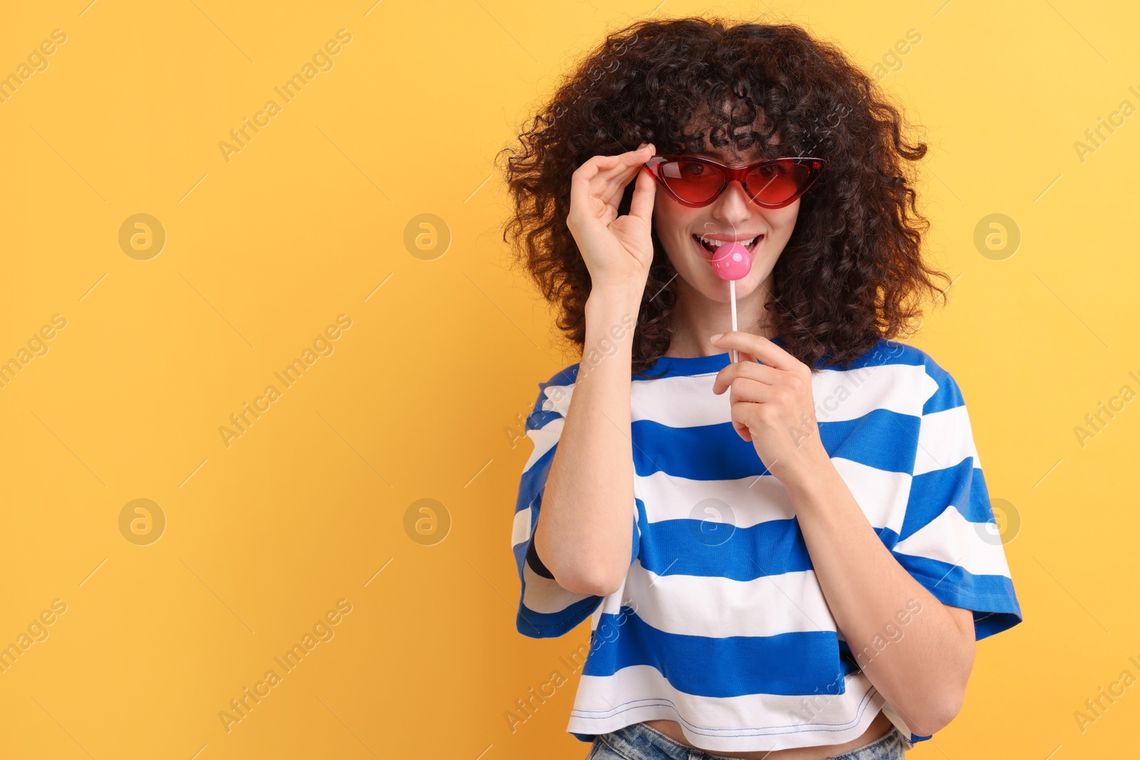 Photo of Beautiful woman in sunglasses with lollipop on yellow background, space for text