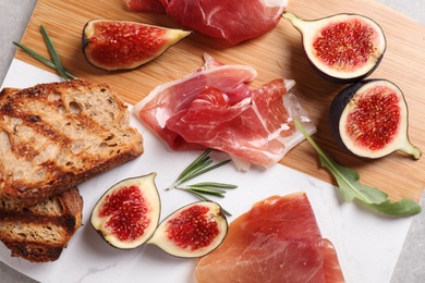 Photo of Delicious ripe figs, prosciutto and toasted bread served on board, top view