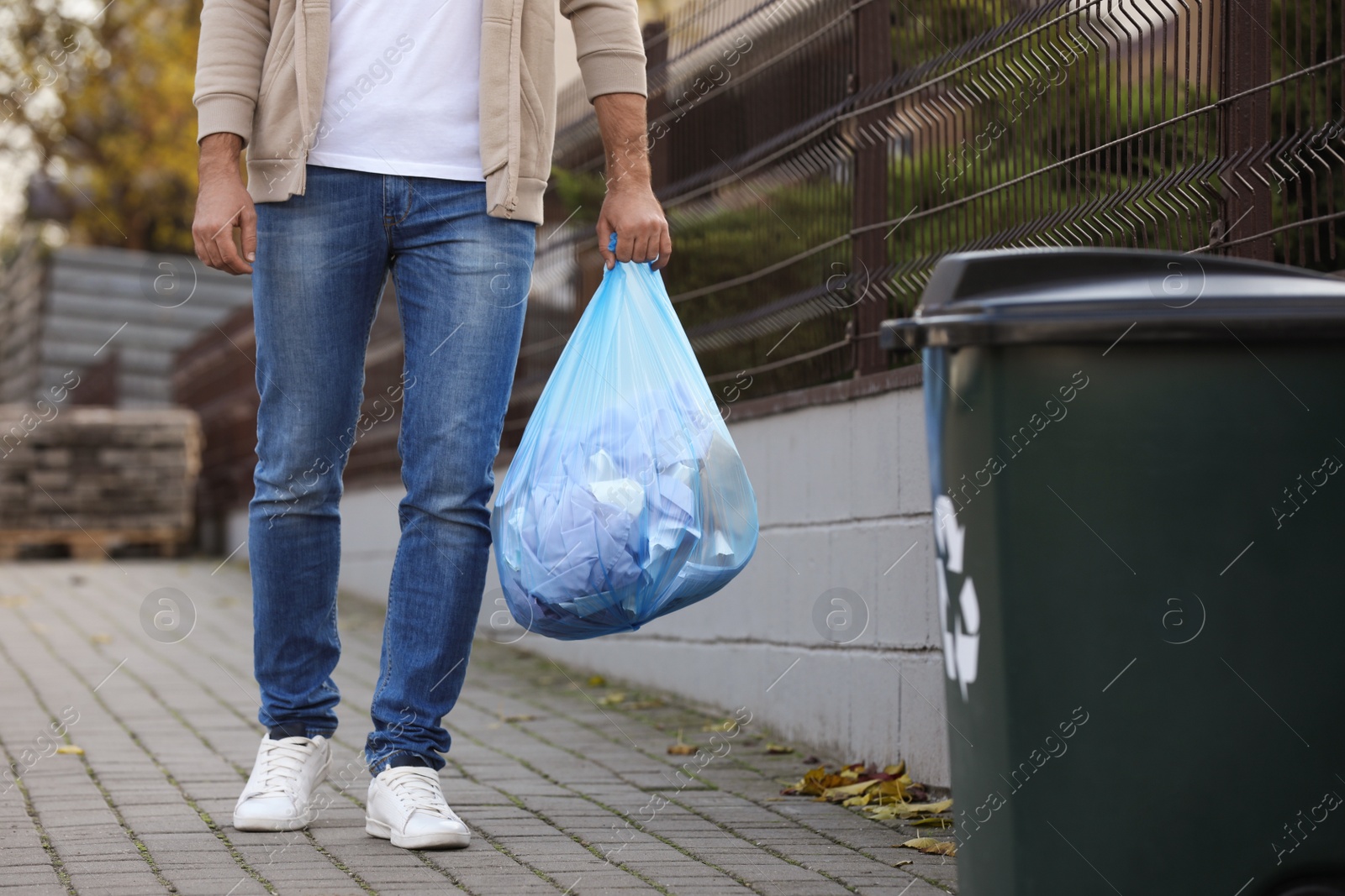Photo of Man carrying garbage bag to recycling bin outdoors, closeup