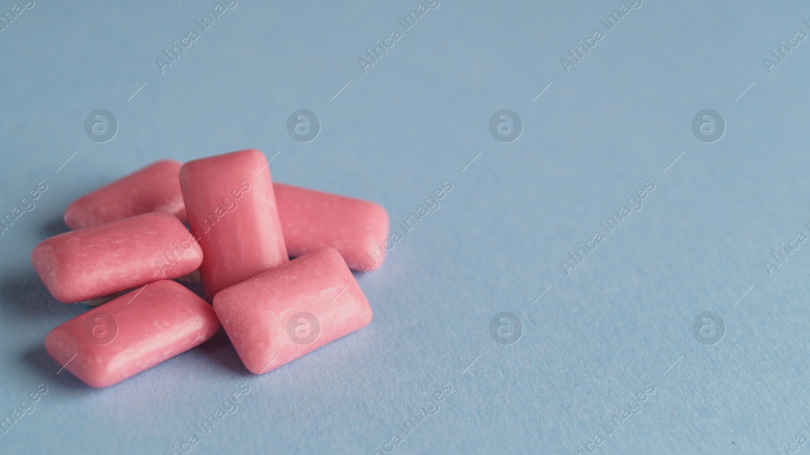 Photo of Heap of tasty sweet chewing gums on light blue background. Space for text