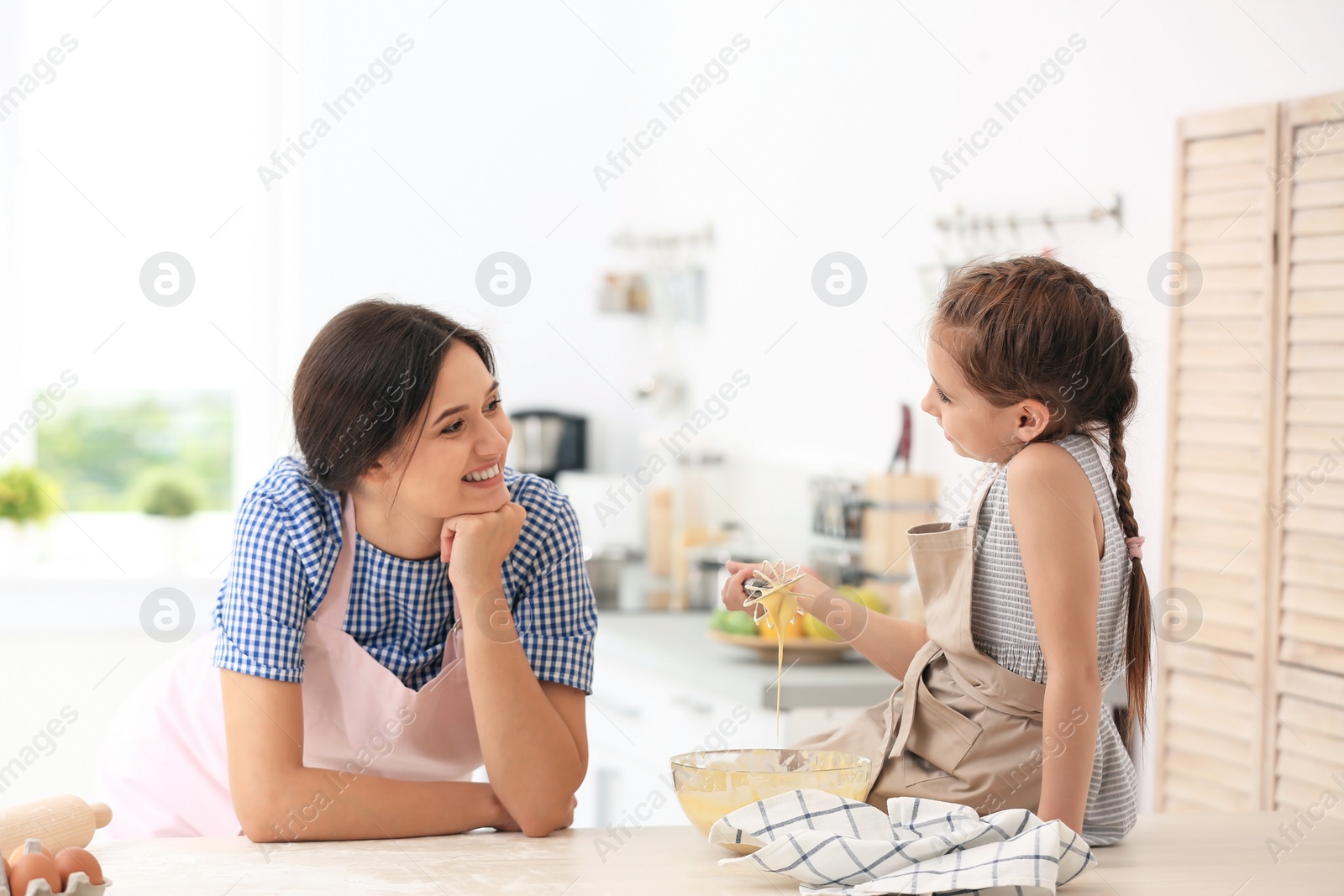 Photo of Mother and her daughter making dough at table in kitchen