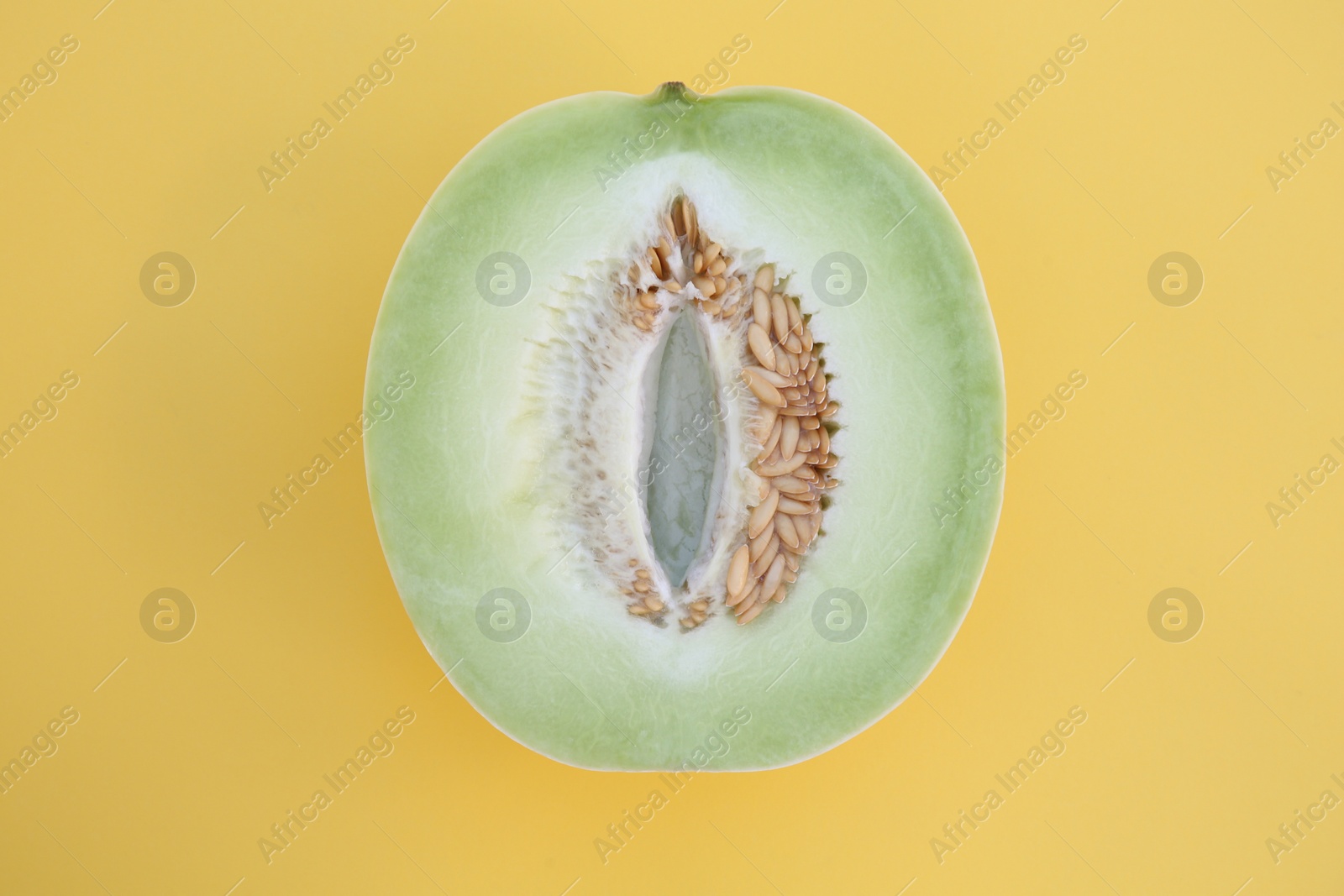 Photo of Half of fresh ripe honeydew melon on yellow background, top view