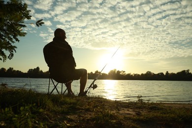 Photo of Fisherman with rod sitting on folding chair and fishing at riverside, space for text