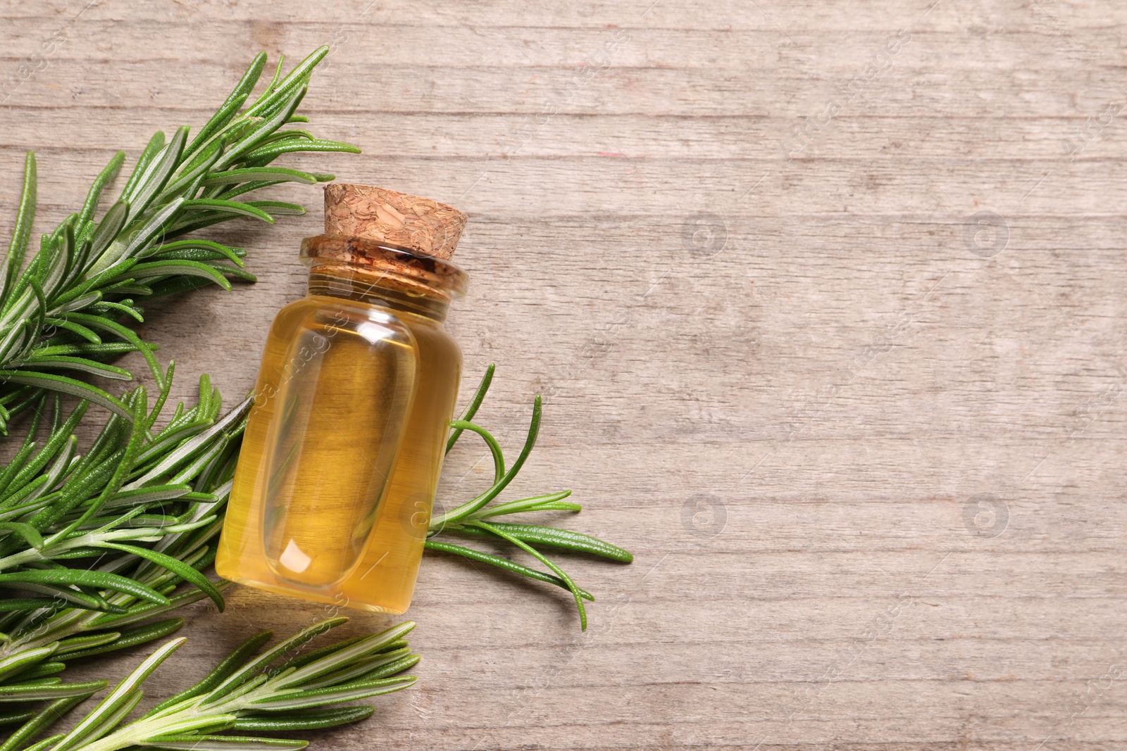 Photo of Bottle of essential oil and fresh rosemary on wooden table, flat lay. Space for text