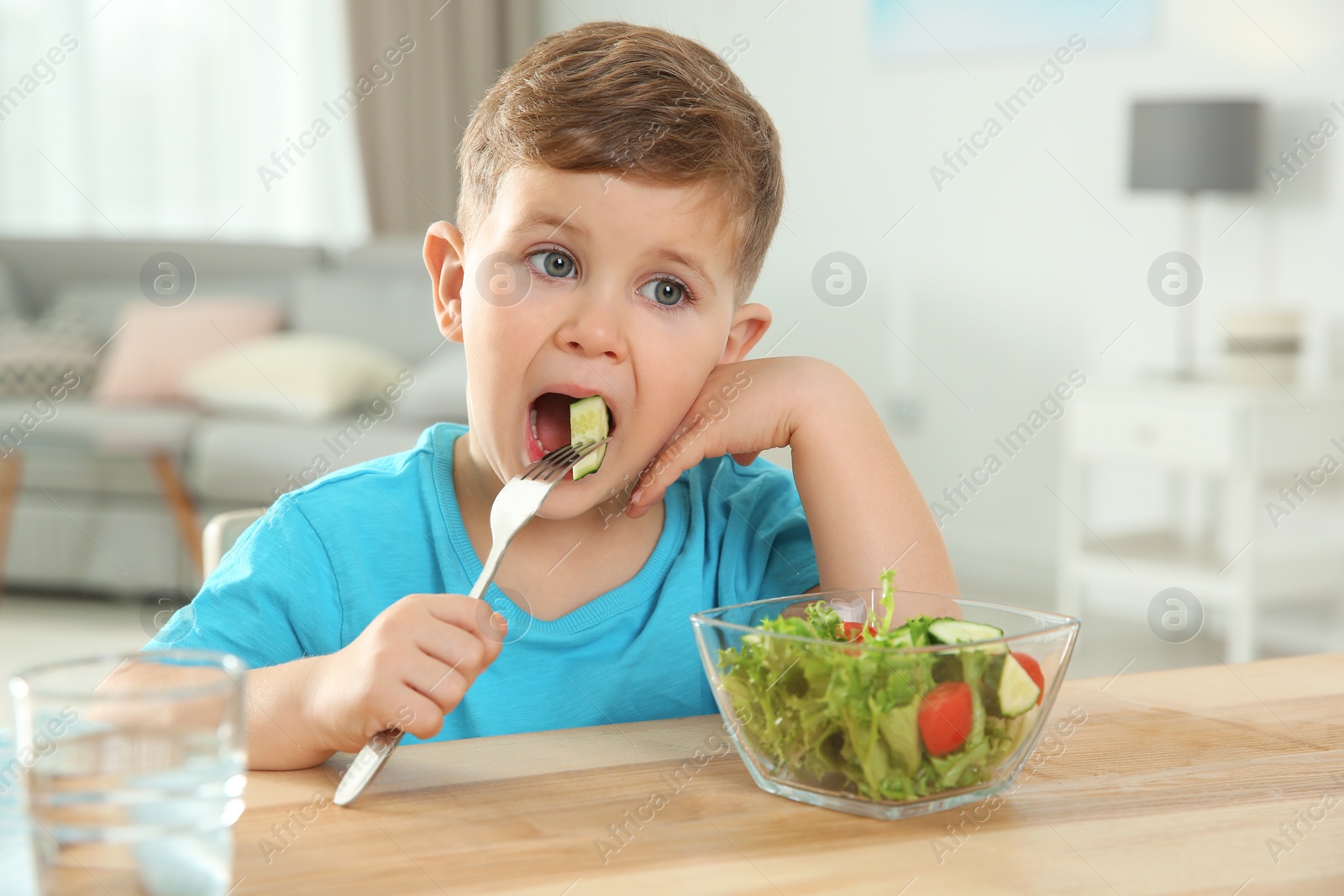 Photo of Adorable little boy eating vegetable salad at table in room