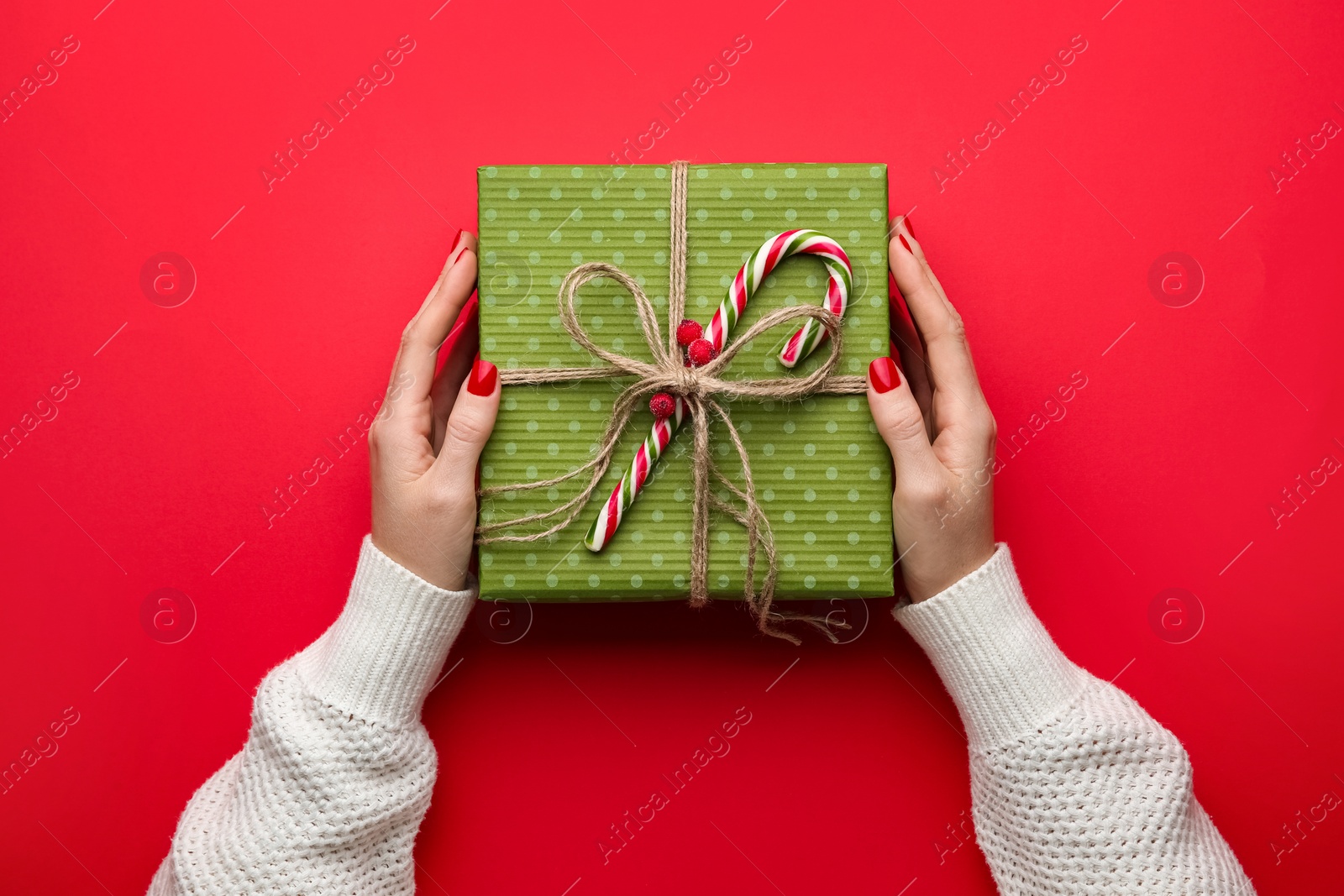 Photo of Woman holding Christmas gift box on red background, top view