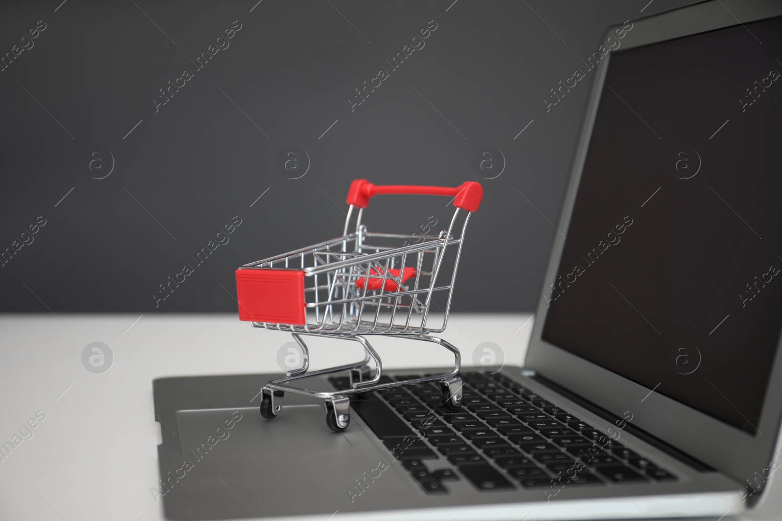 Photo of Internet shopping. Laptop with small cart on table against grey background