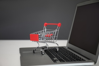 Internet shopping. Laptop with small cart on table against grey background