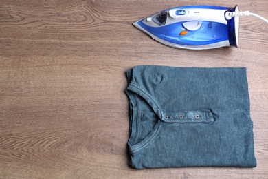 Photo of Flat lay composition with folded clothes and iron on wooden table. Space for text