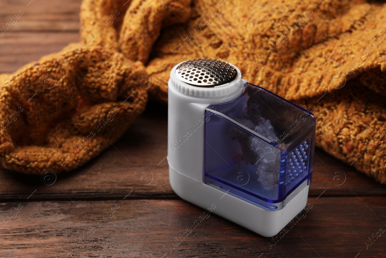 Photo of Modern fabric shaver with fuzz and orange knitted sweater on wooden table, closeup