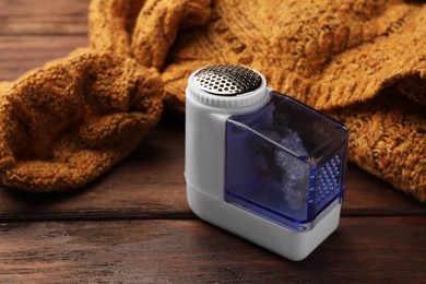 Photo of Modern fabric shaver with fuzz and orange knitted sweater on wooden table, closeup