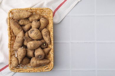 Photo of Tubers of turnip rooted chervil in wicker basket on white tiled table, top view. Space for text
